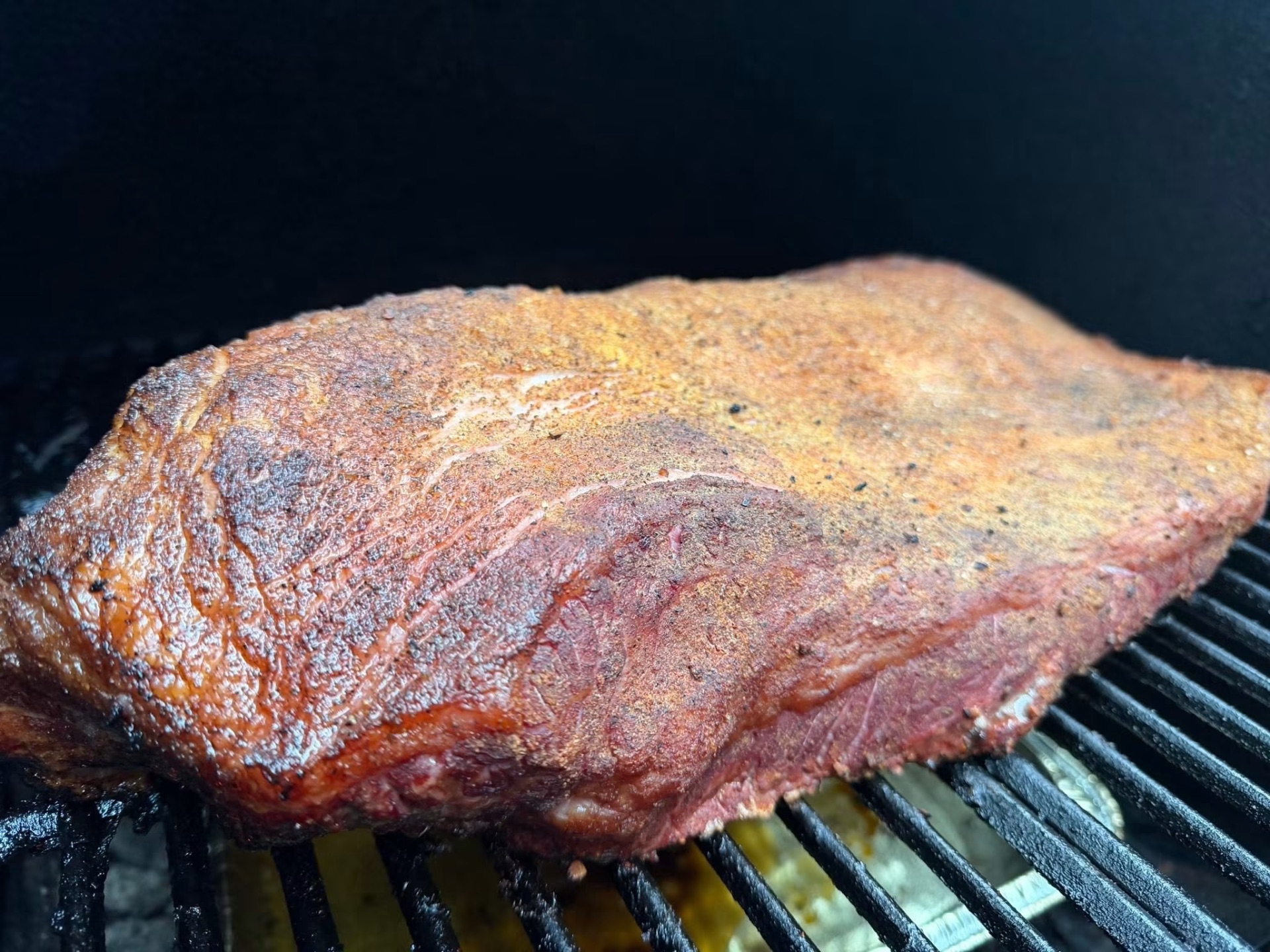 Whole seasoned brisket resting on the smoker grates